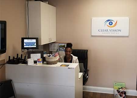 The image shows an individual seated at a desk inside an office space with a sign for Clear Vision.