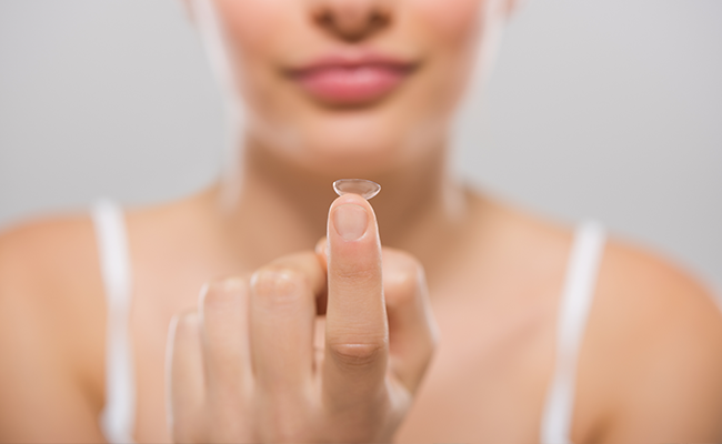 A woman s hand holding an oval-shaped object against her cheek, with her fingers touching her skin.
